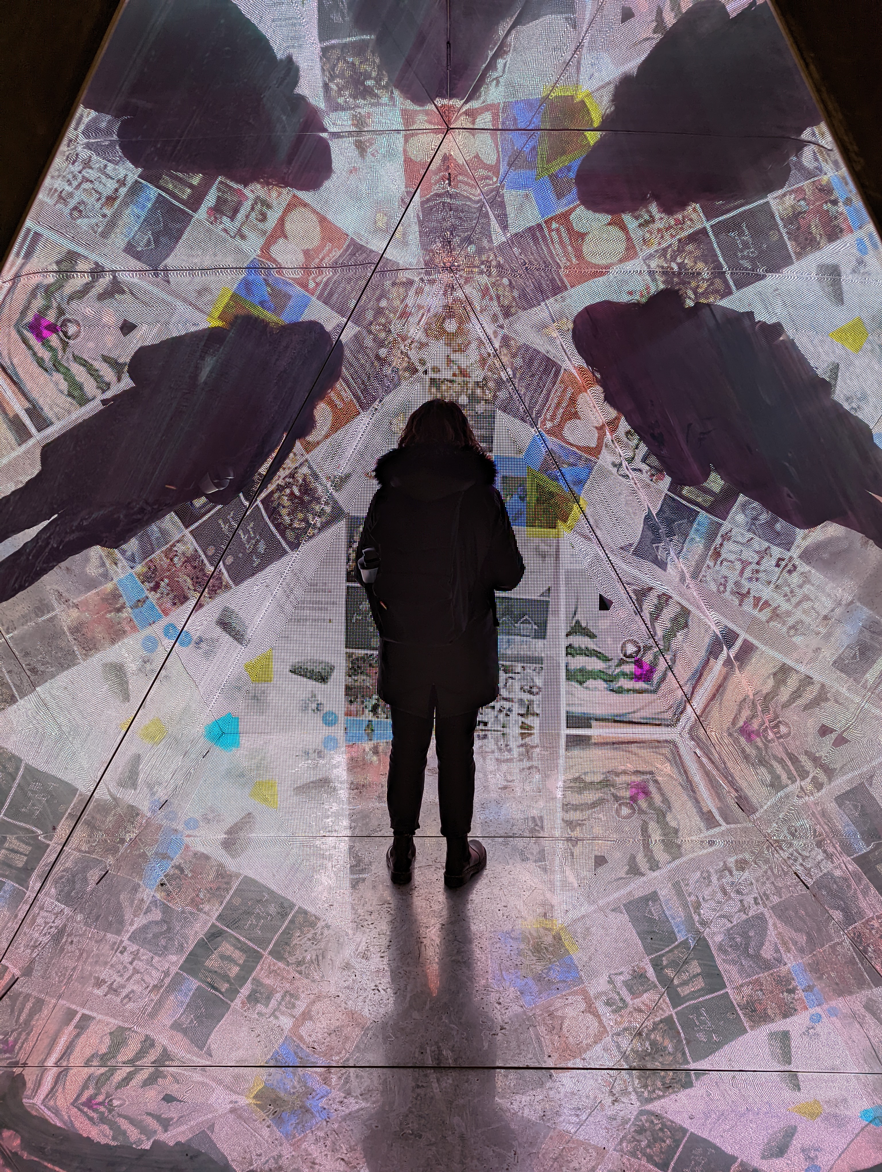 A 3-D interactive art piece at the centre Eaton in Montreal showcasing the immersive nature of social media using a triangle shape to house mirrors and a projection giving hte illusion of depth.